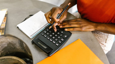 Close-up view of a person typing on calculator next to papers.