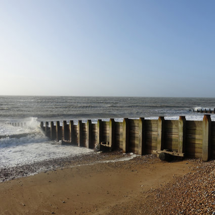 A beach groyne, made of wood, with a sandy and pebbley beach. It's a nice day