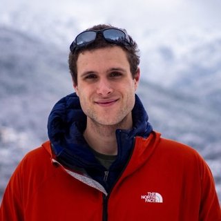 Headshot of person wearing red jacket in snowy environment.