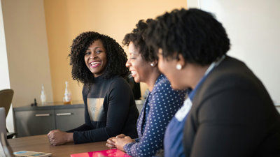 Three people smiling while sitting in a row at a wooden table in an office environment.
