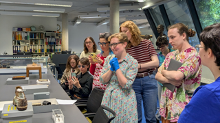 Six people standing up around a table and observing some Collections items.