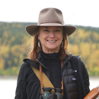 Headshot of Roseann Hanson. She's in the outdoors, wearing a fedora and binoculars.