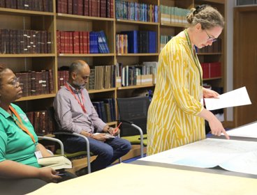 Three people in library making notes and looking at maps.