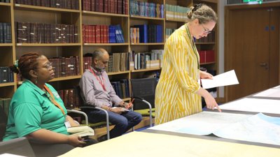 Three people in library making notes and looking at maps.