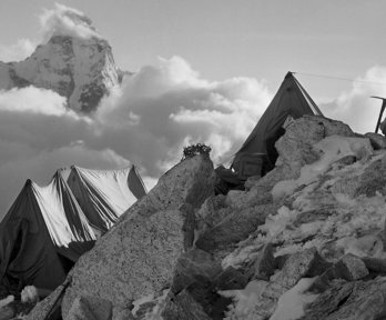 Tent perched on a rocky mountainside with Ama Dablam seen in distance.