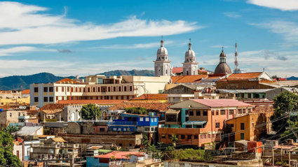 A cluster of buildings of different heights and shapes closely packed together. There are three domed spires and a telecommunications tower that are taller than the other buildings.