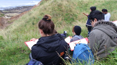 Pupils sitting on a sloped hill doing fieldwork and writing notes