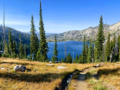 Mountaious feilds, littered with trees surround a large clear blue lake.