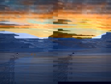Snow capped mountain with people on snow mobiles and a sunset sky