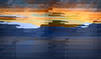 Snow capped mountain with people on snow mobiles and a sunset sky