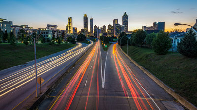 Timelapse of cars on a suburban highway creating light trails leading to a city at golden hour.