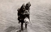 Porters fording a river while carrying a dog.