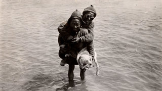 Porters fording a river while carrying a dog.