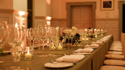 A close-up of glassware and tableware on a formal banquet table in a grand main hall. 