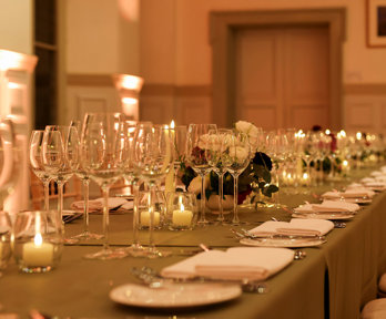 A close-up of glassware and tableware on a formal banquet table in a grand main hall.