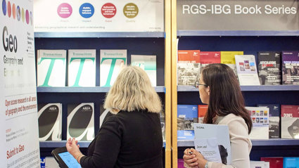 Two people standing in front of a bookcase filled with various Society journal publications such as Transactions, Geo and Area.