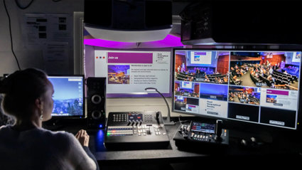 A person sat at a desk working in the recording booth of a lecture theatre.