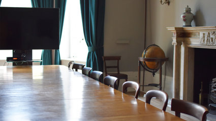Stately looking meeting room with a large wooden table, tv screen and globe.