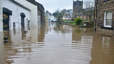 A pub, a church and several other buildings stand flooded up to their first floor windows on Old Main Street, Bingley, UK.