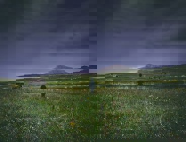 A boy in a field looking out over a stormy sky