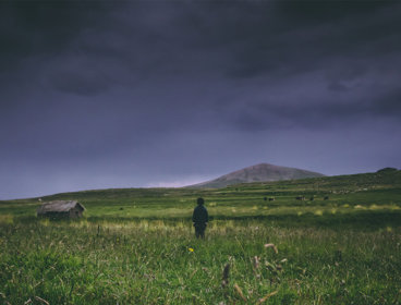A child in a field looking out over a stormy sky.