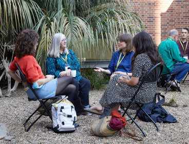 Four conference delegates seated on foldable chairs outside chatting.