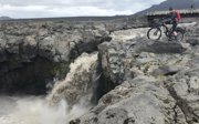 Person on a bicycle on top of rocks overlooking a waterfall.
