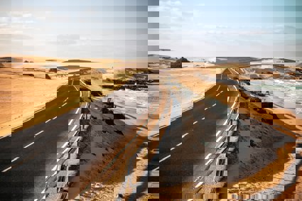 Long black asphalt road with sand dunes and beach to the side