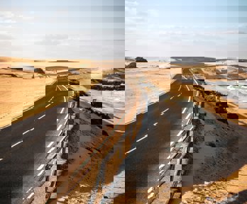 Long black asphalt road with sand dunes and beach to the side