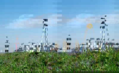 A surveyor carrying out point collection research in a field with a city in the background.