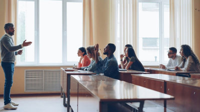 Students sitting at desks listening to someone standing in front and talking.