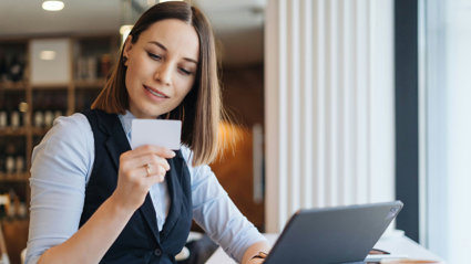 Person looking at a business card whilst sitting at a desk with a laptop.