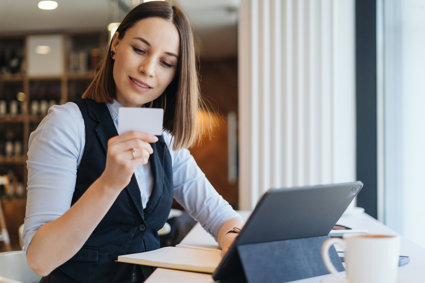 Woman looking at a business card whilst sitting at a desk with a laptop