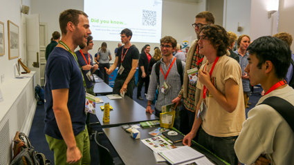 People at a conference networking with an exhibitor standing behind a table.