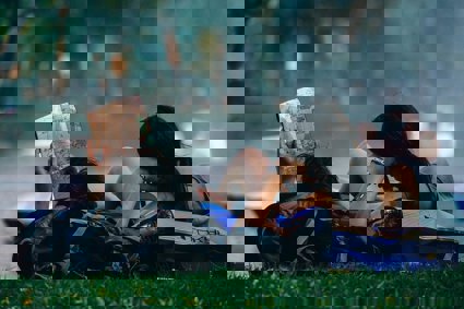 Two people lay down on the grass looking at a map whilst they both rest their heads on their backpacks