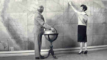 Historic photograph of two people standing in front of large map and with globe.