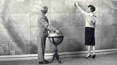 Historic photograph of two people standing in front of large map and with globe.