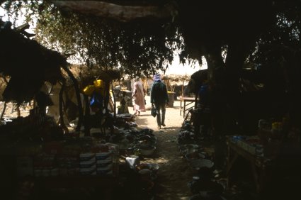 A man walks under a canopy covering a marketplace into the sunlight 