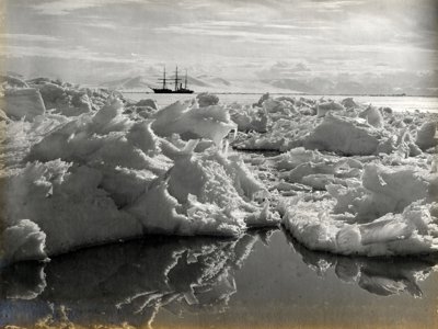 Black and white photo taken in Antarctica of ice in the foreground and a large vessel on the water in the background