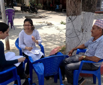 Three people sat on blue plastic chairs in a circle conversing and taking notes.