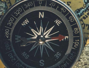A black compass pointing east, placed on a yellow 'old style' map background.