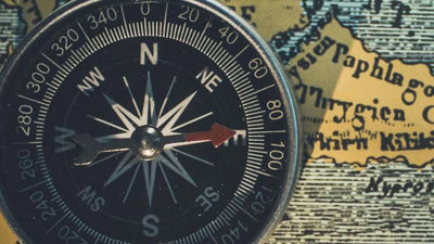 A black compass pointing east, placed on a yellow 'old style' map background.