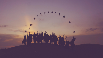 Group at sunset throwing graduation caps in the air