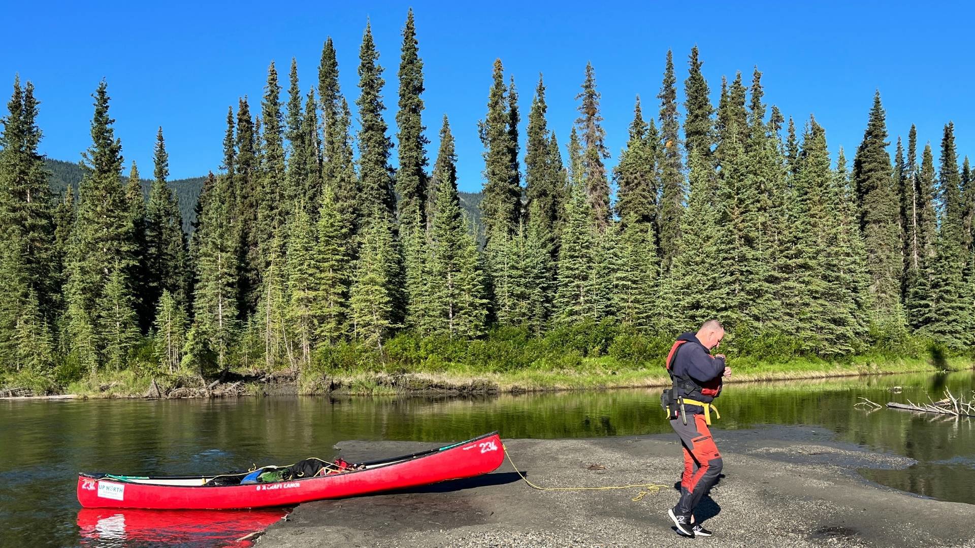 A person walking away from a canoe along a river bank in the forest. 