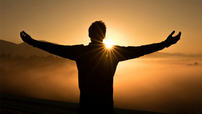 Silhouette of person standing in front of golden sunset.