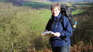 A woman in walking gear holding a map and trekking in nature.