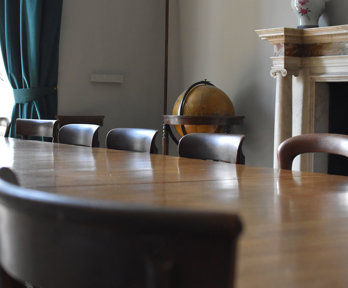 Close up of a large table and chairs in an old and stately meeting room. 