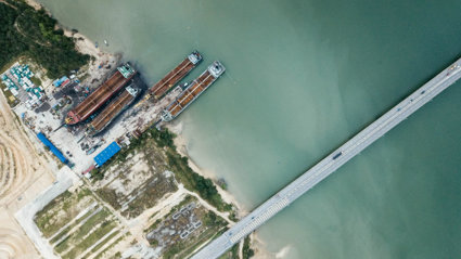 River with a harbour where empty cargo ships have been docked. On the right is a bridge with a road crossing the river.