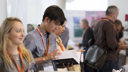 Person wearing a lanyard browsing a book at a publishers stand.