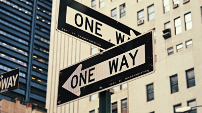 Two road signs perpendicular to each other and both saying one way are in a urban centre.